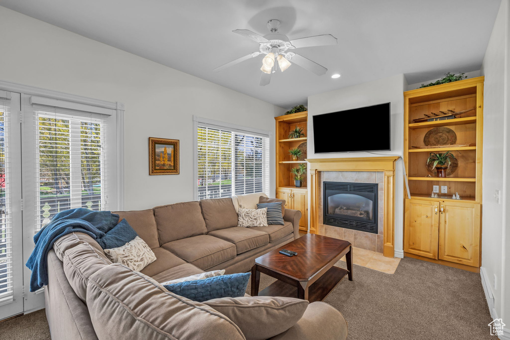 Carpeted living room featuring built in features, ceiling fan, a healthy amount of sunlight, and a tiled fireplace