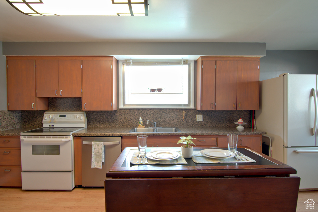 Kitchen with backsplash, light hardwood / wood-style flooring, white appliances, and sink
