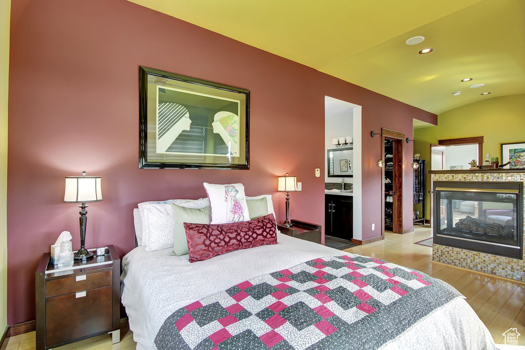 Bedroom with ensuite bathroom, vaulted ceiling, a multi sided fireplace, a walk in closet, and light wood-type flooring