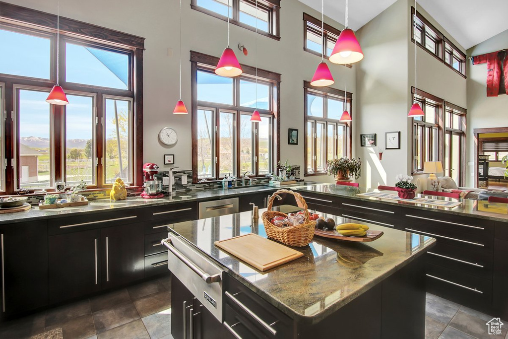 Kitchen featuring dark tile floors, a towering ceiling, a kitchen island, sink, and pendant lighting