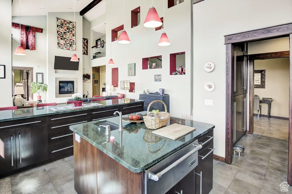 Kitchen with hanging light fixtures, a fireplace, light tile floors, dark stone countertops, and an island with sink