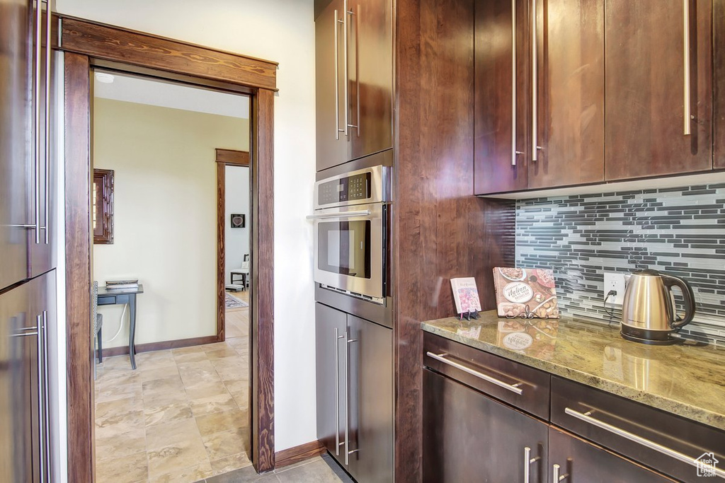 Kitchen featuring tasteful backsplash, stainless steel oven, light tile floors, and light stone countertops