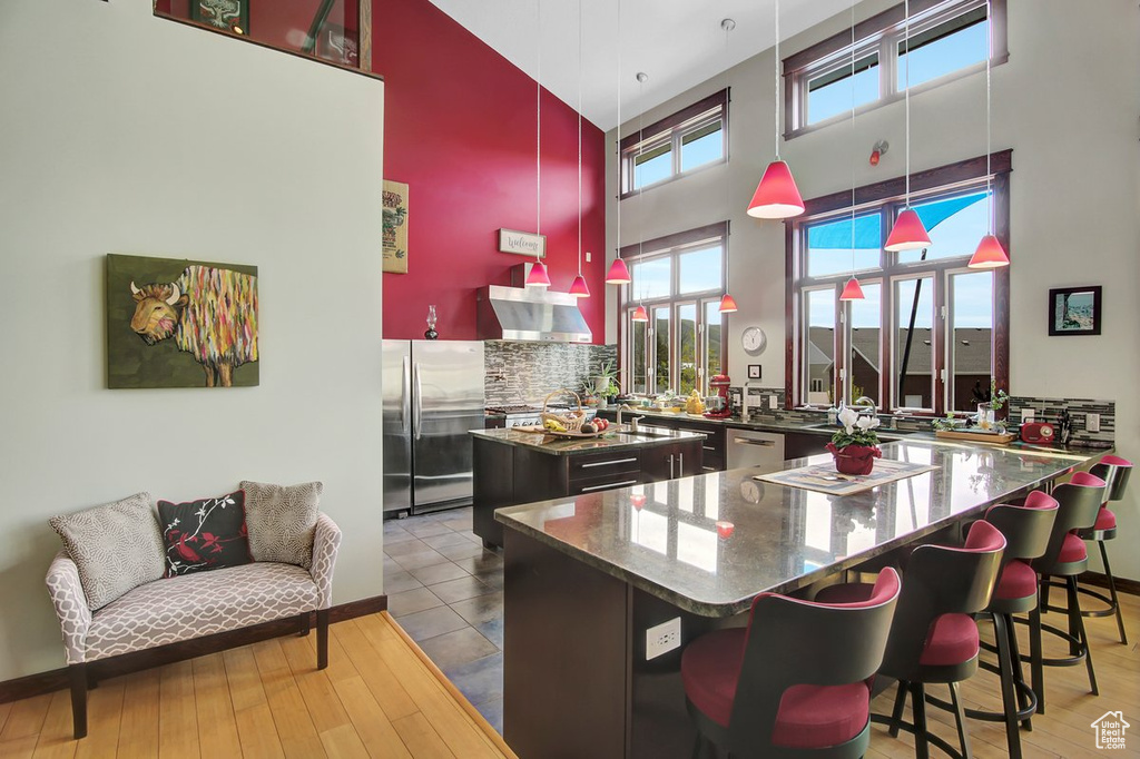 Kitchen featuring appliances with stainless steel finishes, a towering ceiling, a kitchen island, tasteful backsplash, and dark stone countertops