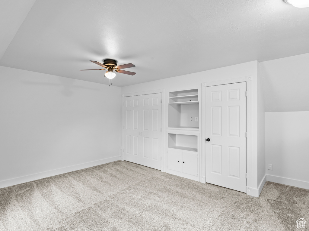 Unfurnished bedroom featuring light colored carpet, multiple closets, ceiling fan, and lofted ceiling