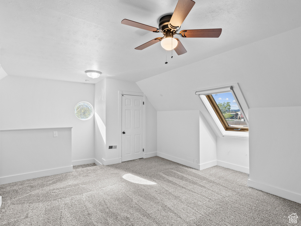 Additional living space with light carpet, lofted ceiling with skylight, and ceiling fan