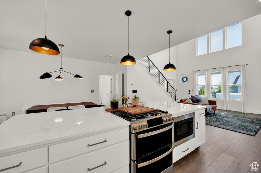 Kitchen featuring appliances with stainless steel finishes, a kitchen island, hanging light fixtures, wood-type flooring, and white cabinets