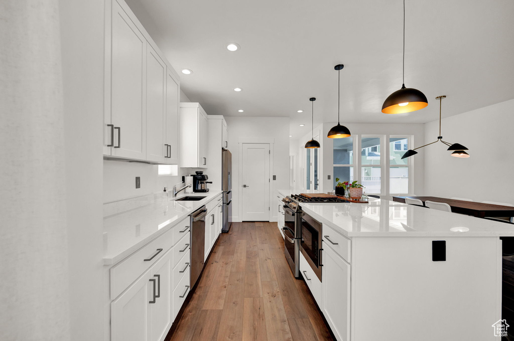 Kitchen with sink, white cabinetry, decorative light fixtures, stainless steel appliances, and hardwood / wood-style flooring