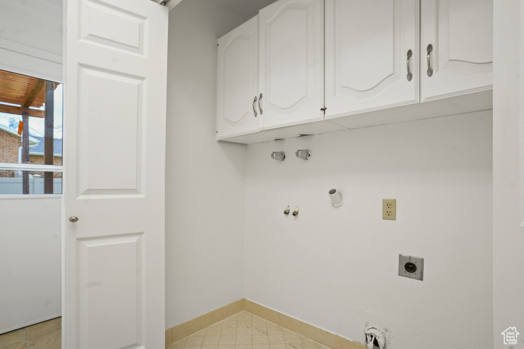 Clothes washing area with hookup for an electric dryer, cabinets, and light tile floors