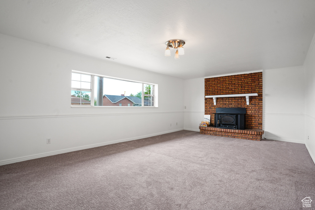 Unfurnished living room featuring a fireplace, crown molding, brick wall, and carpet flooring
