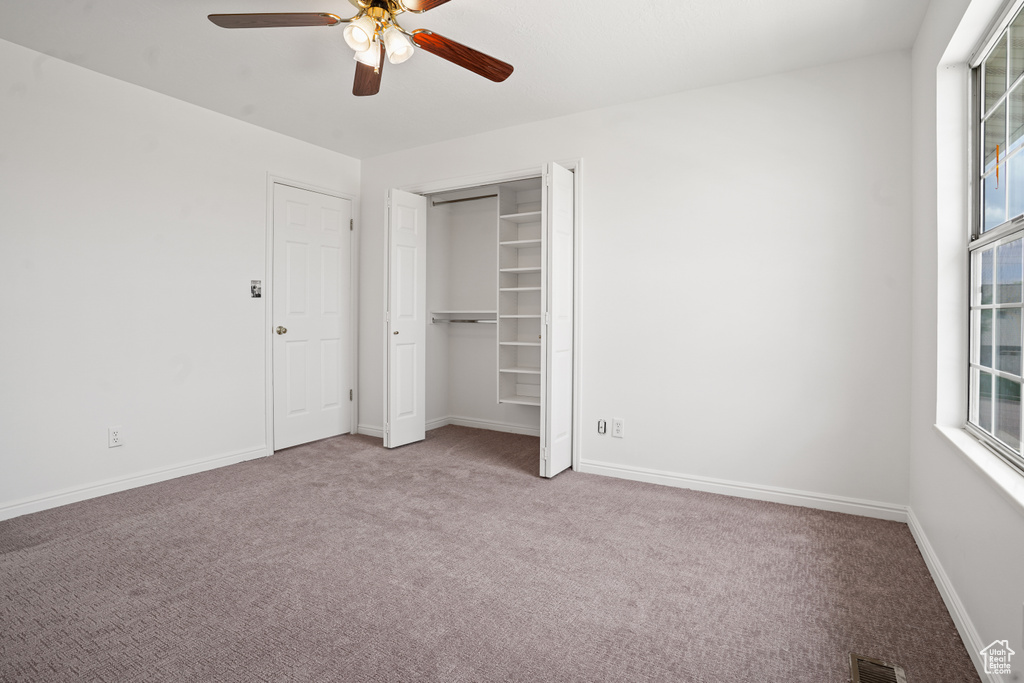Unfurnished bedroom with a closet, multiple windows, ceiling fan, and carpet floors