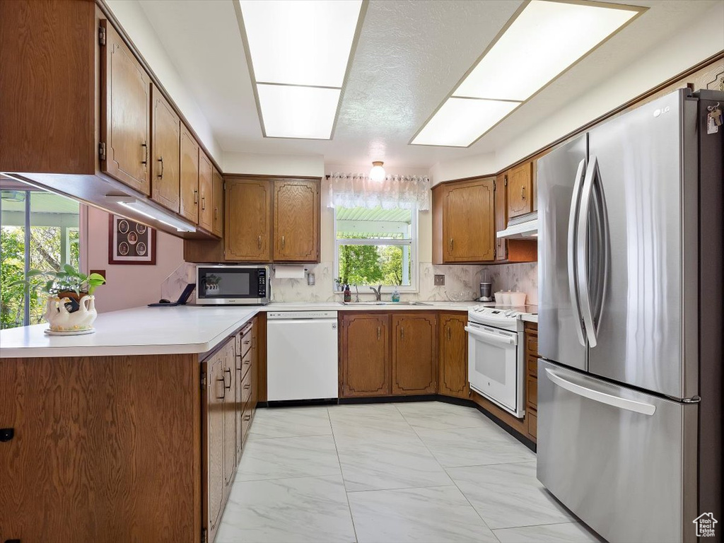 Kitchen featuring sink, backsplash, appliances with stainless steel finishes, and light tile floors