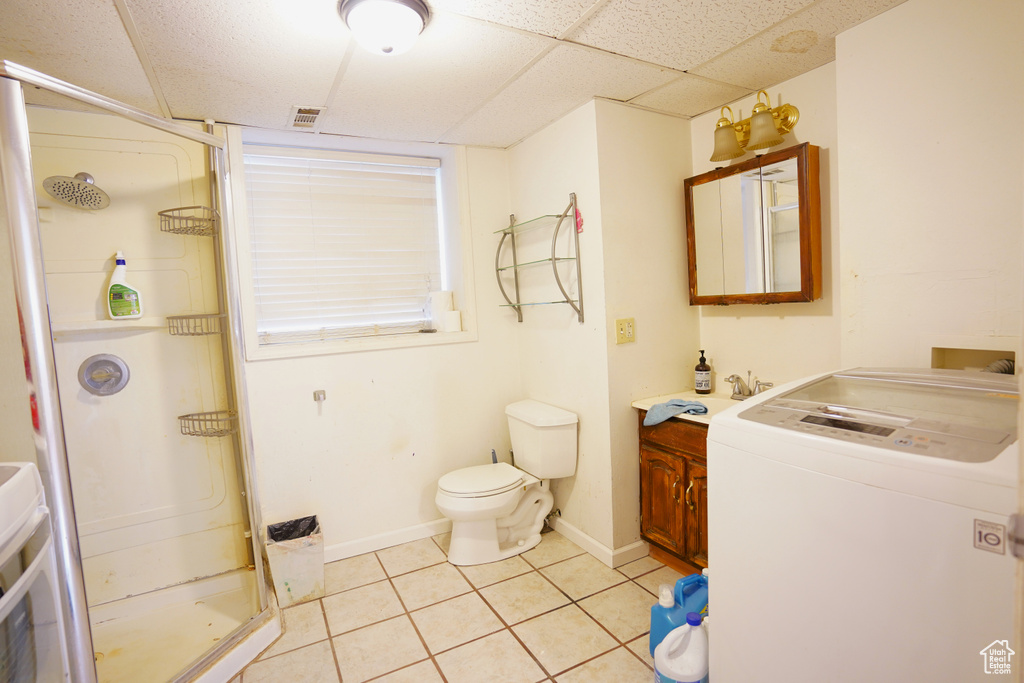 Bathroom featuring tile flooring, a paneled ceiling, washer / dryer, walk in shower, and toilet