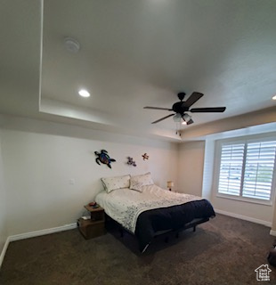 Bedroom with dark colored carpet, ceiling fan, and a raised ceiling