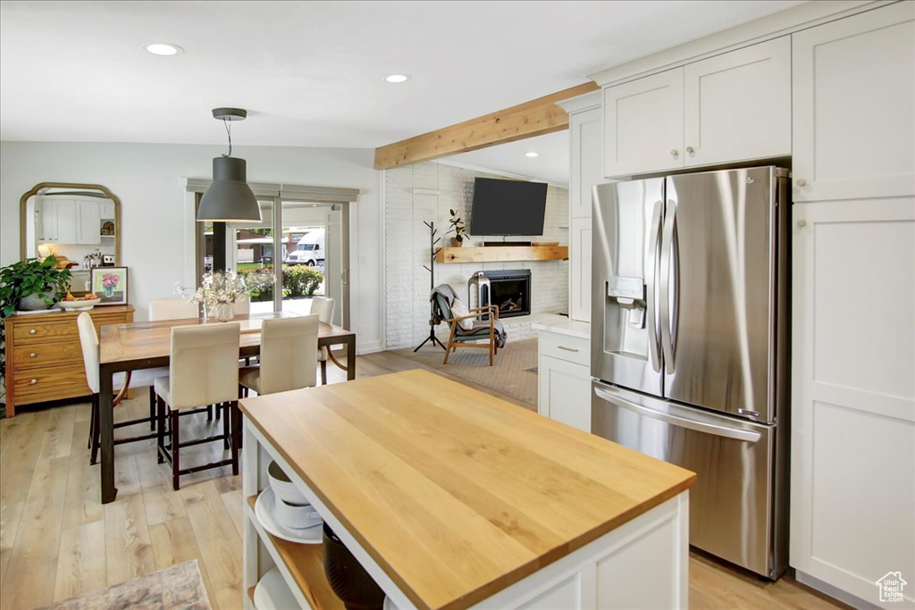 Kitchen featuring hanging light fixtures, a fireplace, white cabinetry, stainless steel fridge with ice dispenser, and light hardwood / wood-style floors