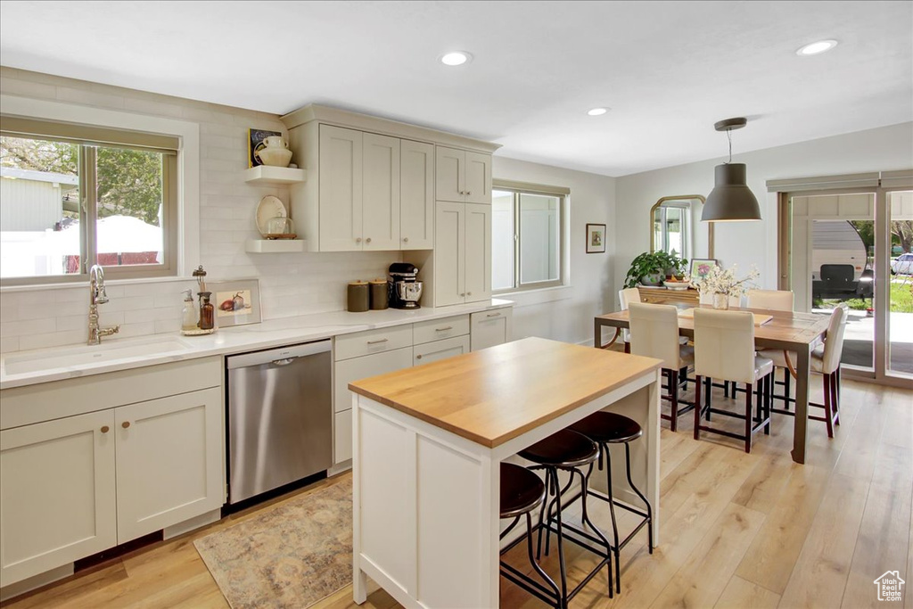 Kitchen with decorative light fixtures, tasteful backsplash, sink, light wood-type flooring, and stainless steel dishwasher