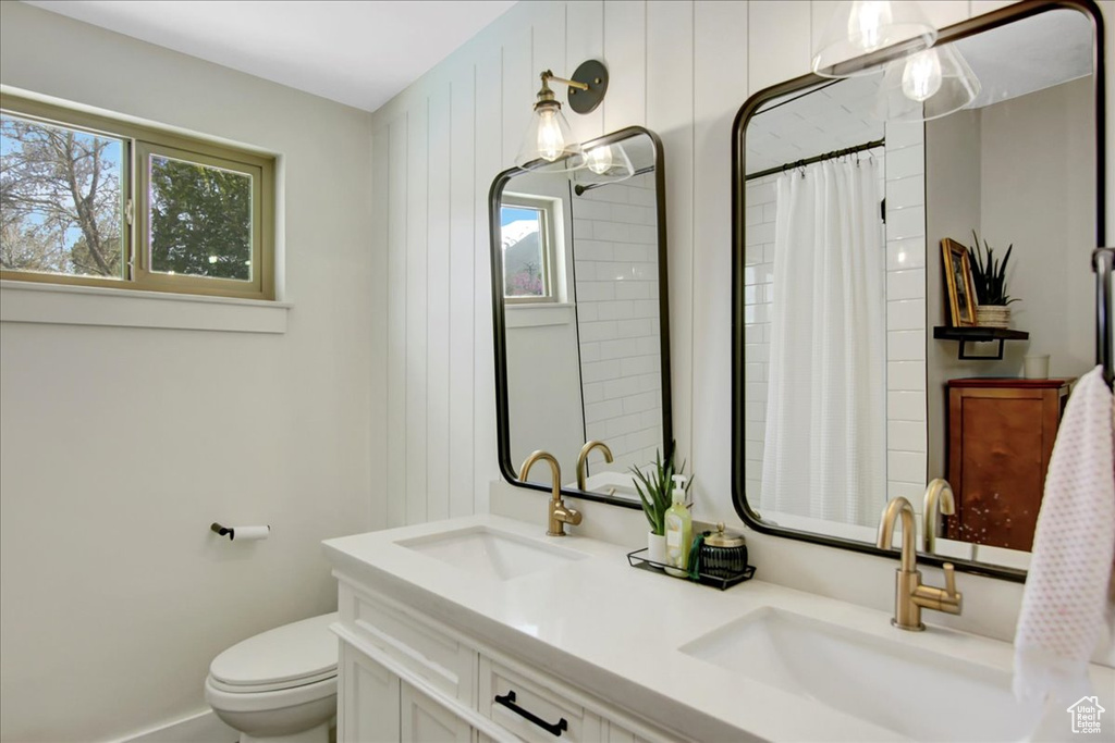 Bathroom featuring vanity with extensive cabinet space, toilet, and double sink
