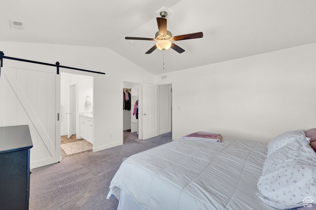 Carpeted bedroom with a barn door, ensuite bath, ceiling fan, lofted ceiling, and a walk in closet