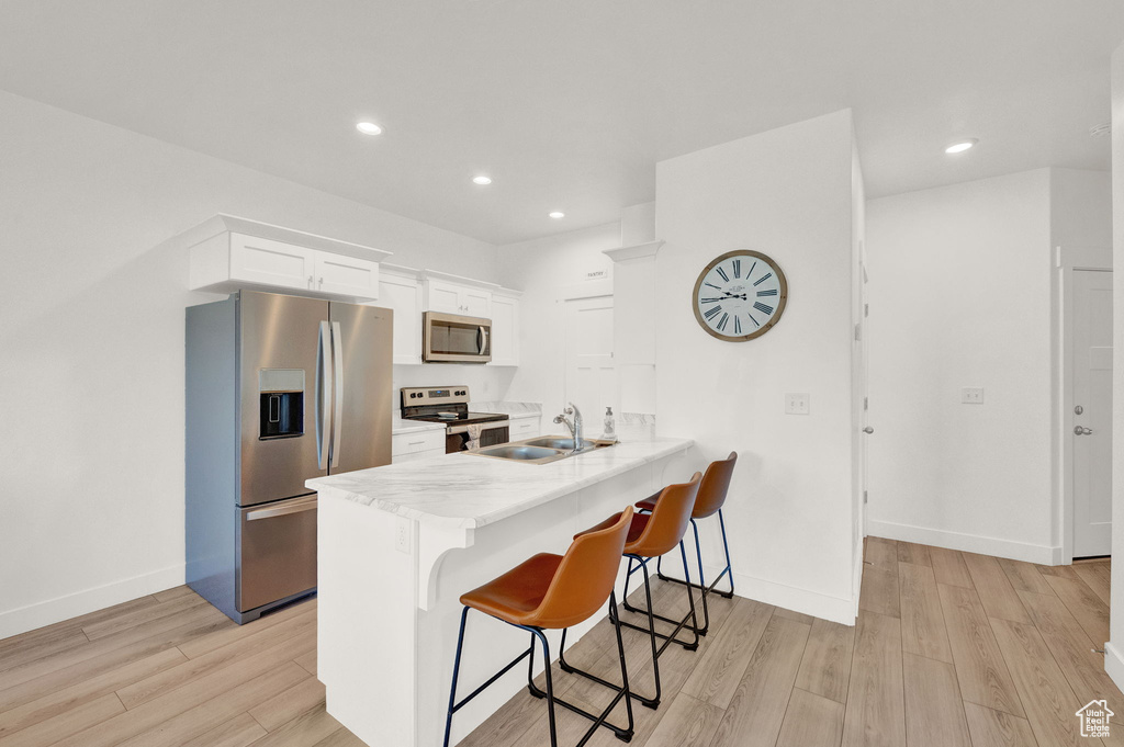 Kitchen with light wood-type flooring, white cabinetry, a breakfast bar area, stainless steel appliances, and kitchen peninsula