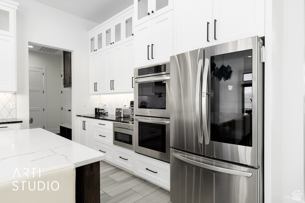 Kitchen featuring white cabinets, appliances with stainless steel finishes, backsplash, and light stone countertops