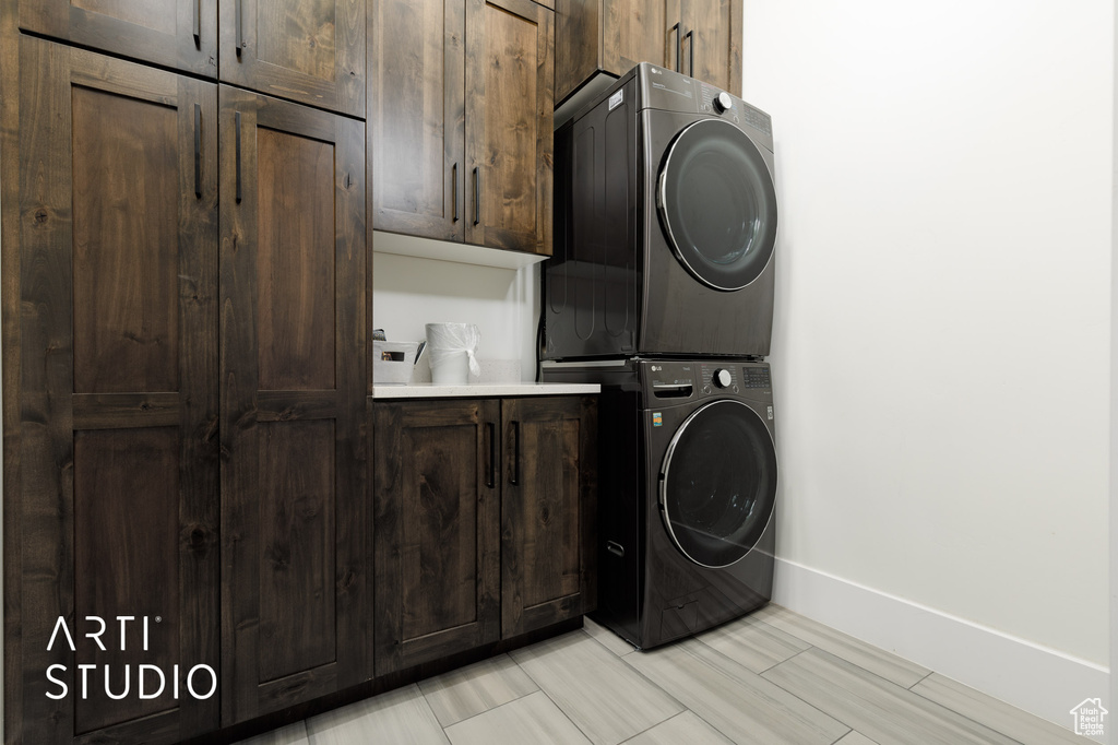 Washroom featuring stacked washer and dryer, cabinets, and light tile floors