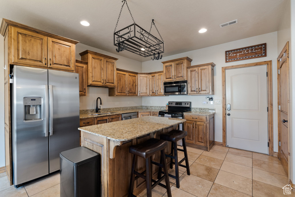 Kitchen featuring appliances with stainless steel finishes, light tile floors, a kitchen island, sink, and light stone countertops