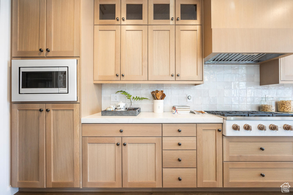 Kitchen featuring light brown cabinets, gas cooktop, premium range hood, stainless steel microwave, and tasteful backsplash