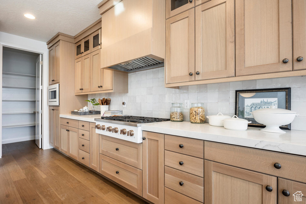 Kitchen featuring tasteful backsplash, stainless steel microwave, wood-type flooring, white gas cooktop, and premium range hood