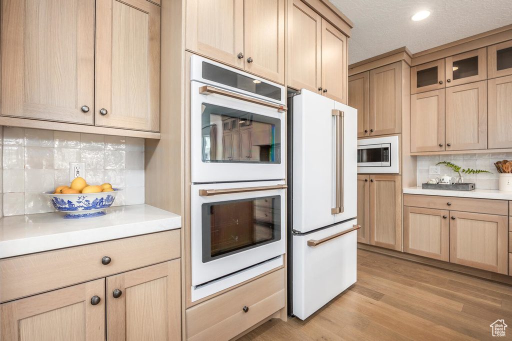Kitchen featuring multiple ovens, light hardwood / wood-style floors, tasteful backsplash, stainless steel microwave, and high end fridge