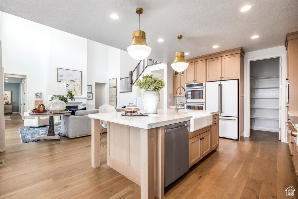 Kitchen featuring appliances with stainless steel finishes, a kitchen island with sink, a textured ceiling, light wood-type flooring, and pendant lighting