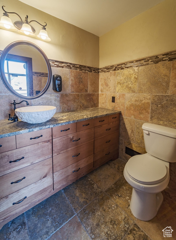 Bathroom with tile flooring, tile walls, vanity, and toilet