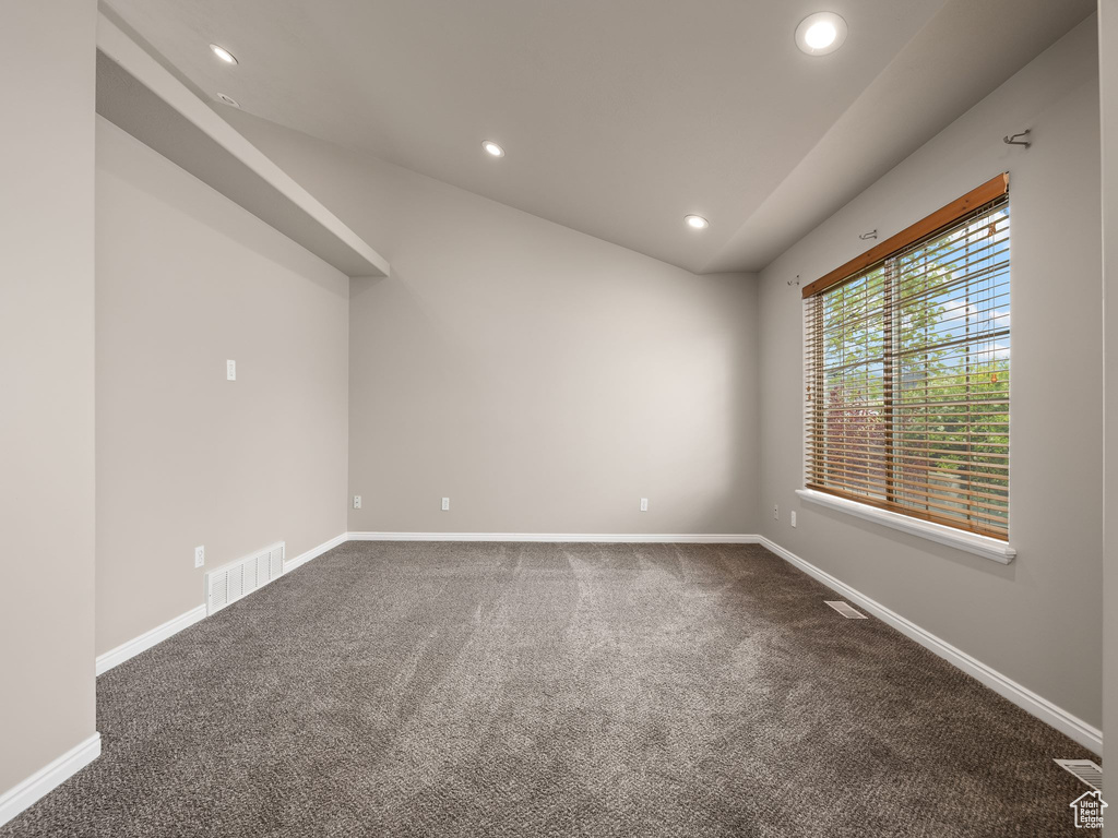 Unfurnished room featuring dark colored carpet and lofted ceiling