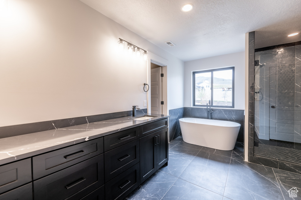 Bathroom featuring a textured ceiling, vanity, tile floors, and plus walk in shower