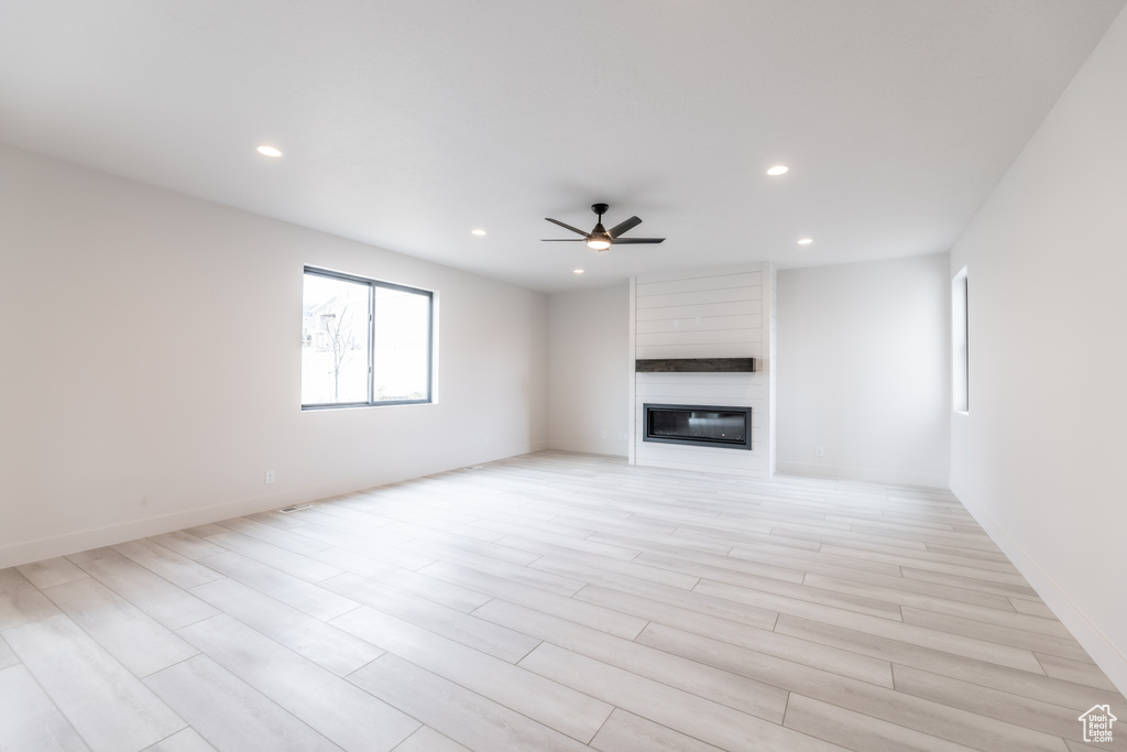 Unfurnished living room with light hardwood / wood-style flooring, ceiling fan, and a fireplace