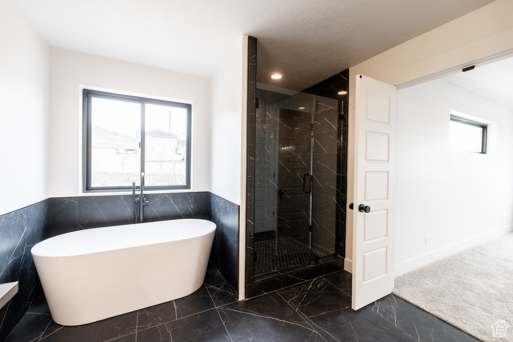Bathroom with tile flooring, tile walls, and separate shower and tub