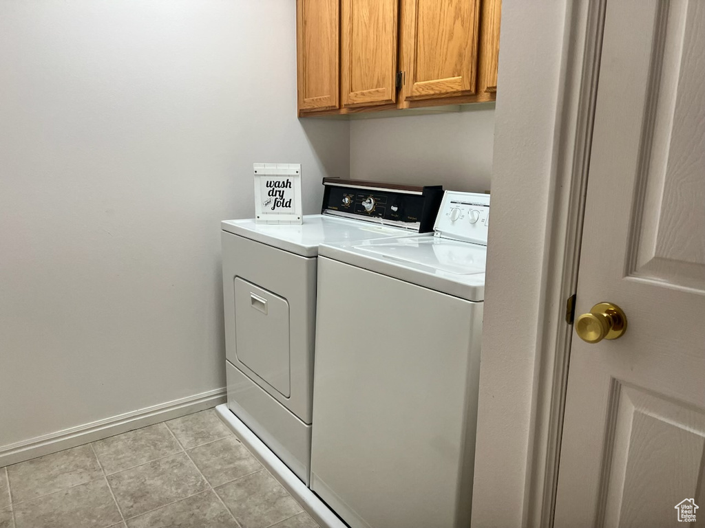 Clothes washing area with light tile flooring, cabinets, and separate washer and dryer