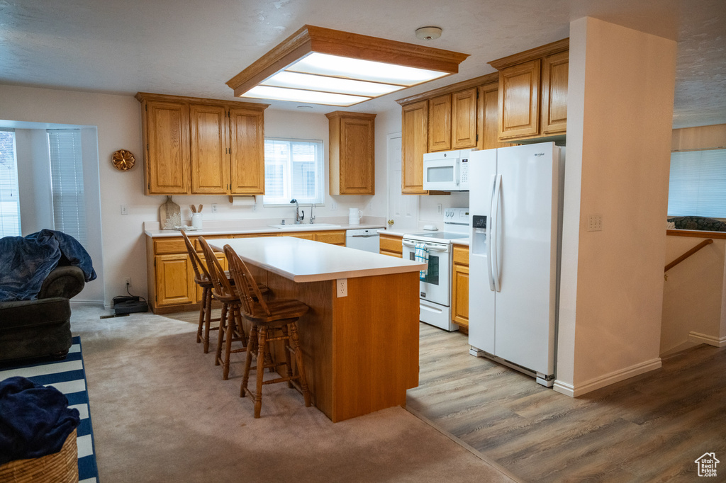 Kitchen featuring a center island, sink, white appliances, a breakfast bar area, and light colored carpet
