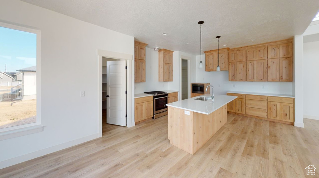 Kitchen with stainless steel appliances, a center island with sink, light brown cabinetry, and light hardwood / wood-style flooring