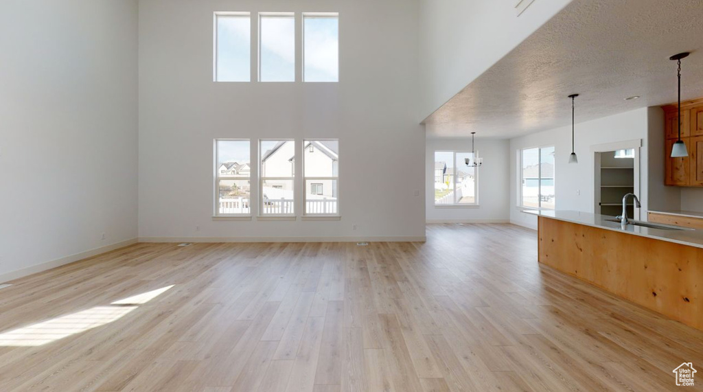 Unfurnished living room with light hardwood / wood-style floors, sink, a towering ceiling, and a notable chandelier