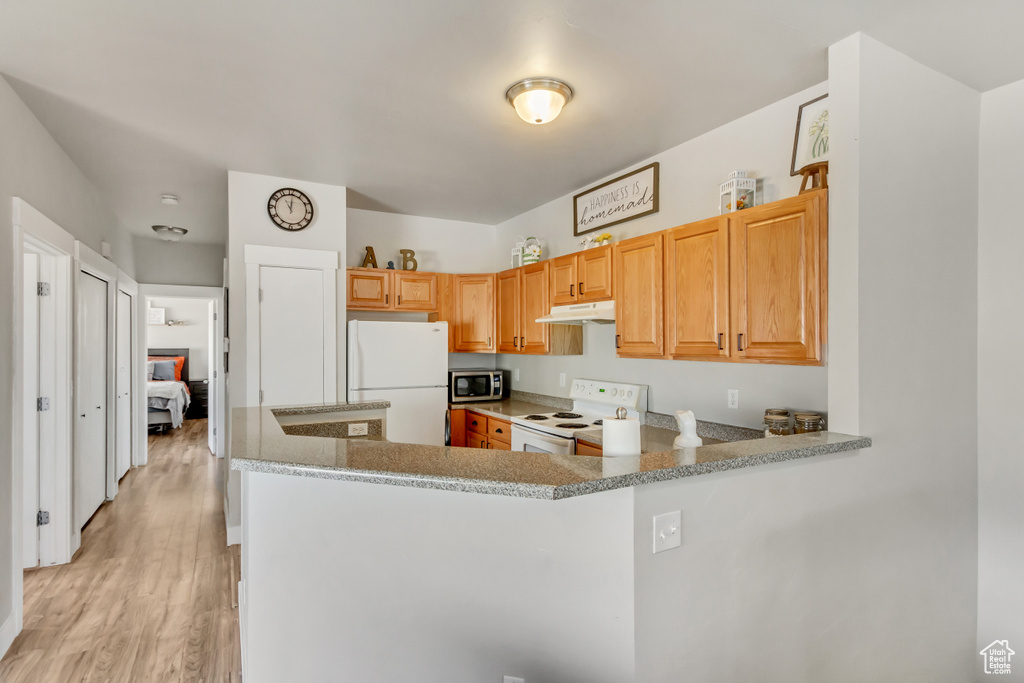 Kitchen with white appliances, kitchen peninsula, light wood-type flooring, and light stone countertops