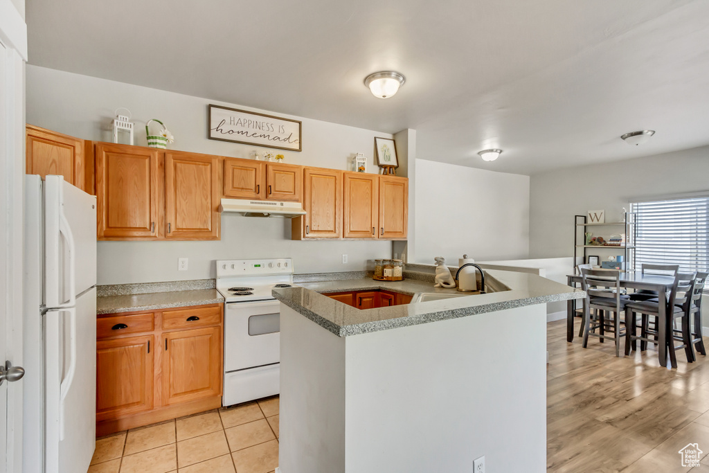 Kitchen with light hardwood / wood-style flooring, white appliances, kitchen peninsula, and sink