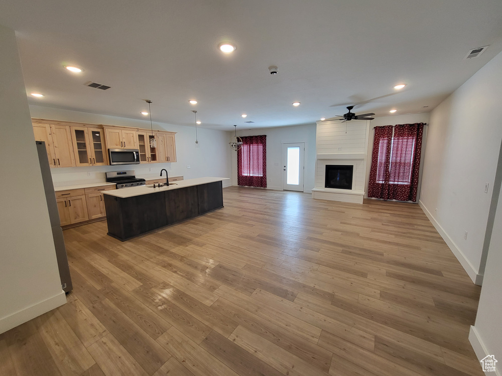 Kitchen with a fireplace, hardwood / wood-style floors, appliances with stainless steel finishes, ceiling fan, and an island with sink
