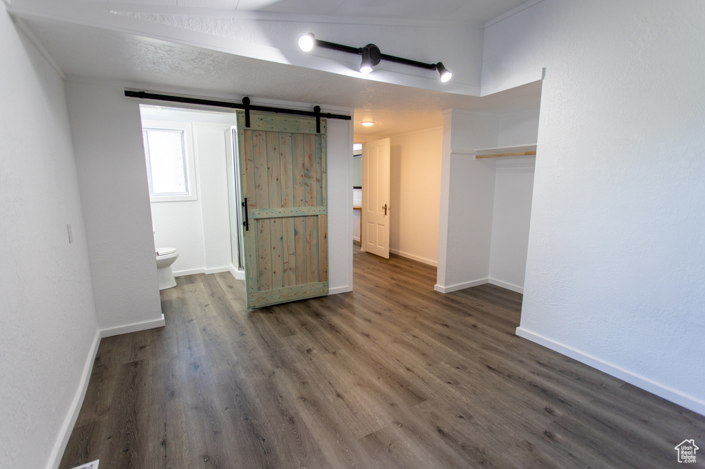 Unfurnished bedroom featuring dark hardwood / wood-style flooring, ensuite bath, and a barn door