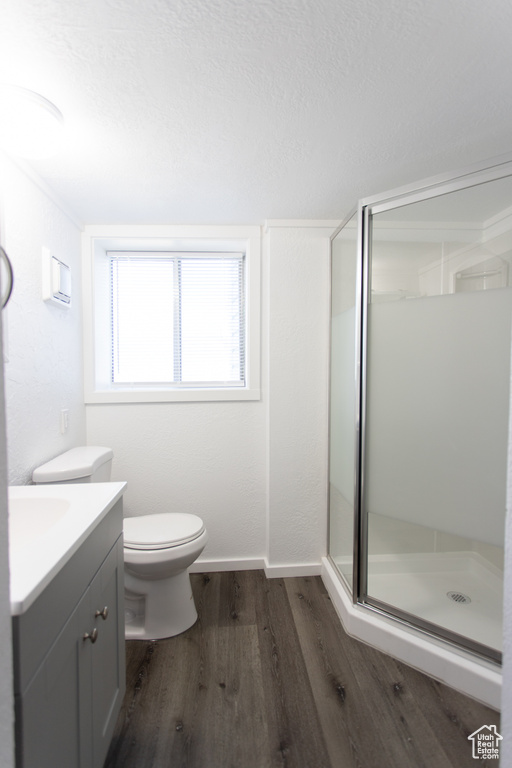 Bathroom with a shower with shower door, vanity, toilet, and hardwood / wood-style flooring