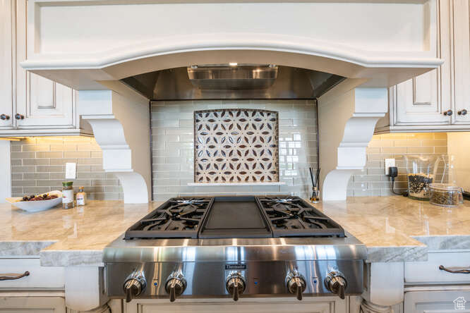 Kitchen featuring tasteful backsplash, wall chimney exhaust hood, and white cabinetry