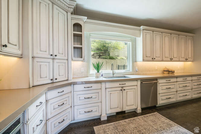Kitchen with stainless steel dishwasher, tasteful backsplash, white cabinetry, dark hardwood / wood-style flooring, and sink