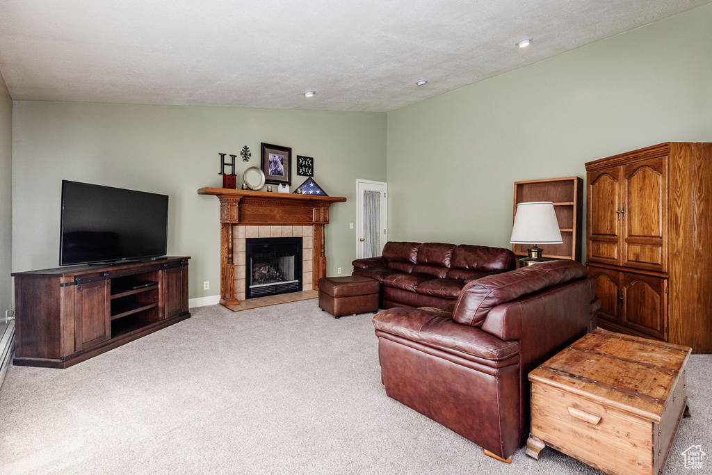 Living room with a tiled fireplace, light carpet, and lofted ceiling