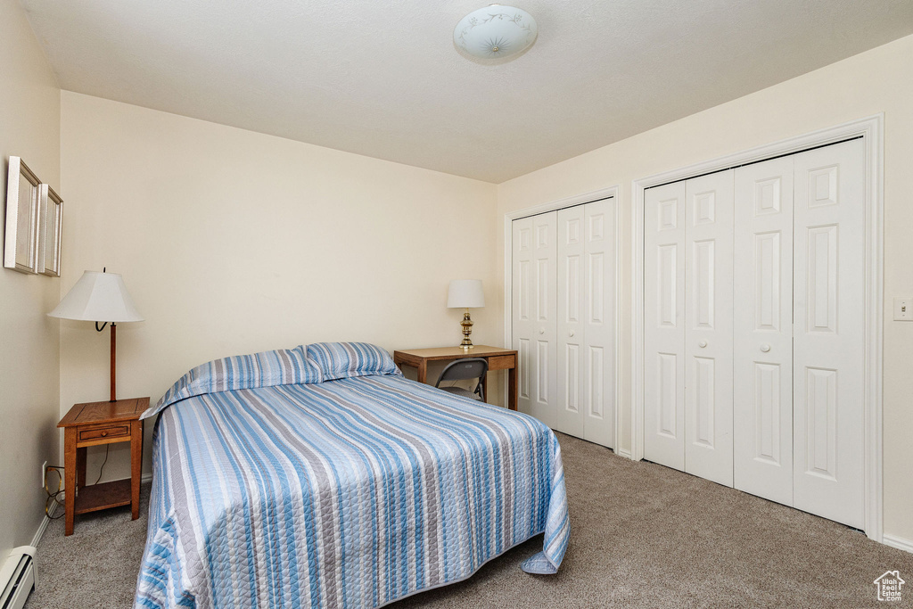 Bedroom with carpet flooring, a baseboard radiator, and multiple closets