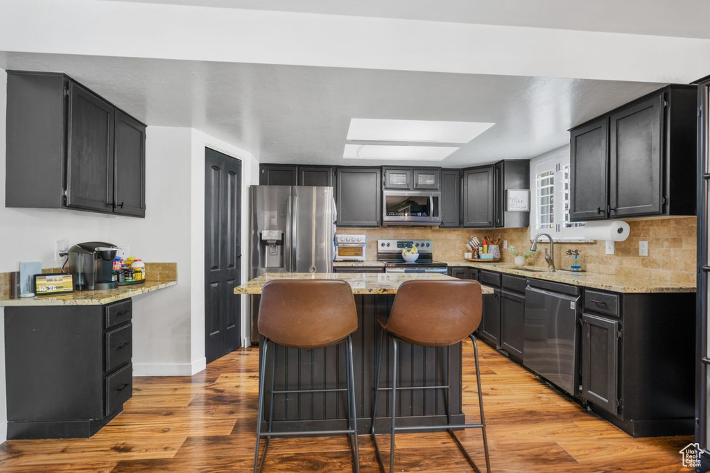 Kitchen featuring light stone countertops, light hardwood / wood-style flooring, stainless steel appliances, tasteful backsplash, and a breakfast bar