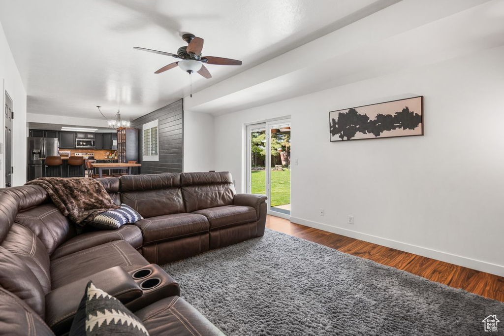 Living room with ceiling fan with notable chandelier and dark hardwood / wood-style floors