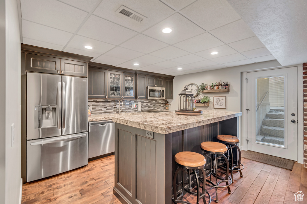 Kitchen featuring backsplash, appliances with stainless steel finishes, a drop ceiling, and light hardwood / wood-style flooring